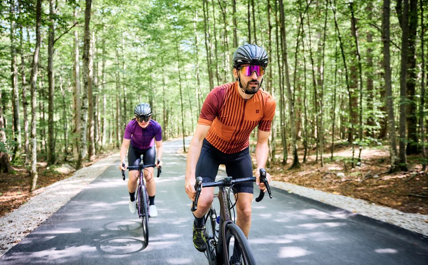 Due ciclisti con casco che pedalano su una strada nella foresta