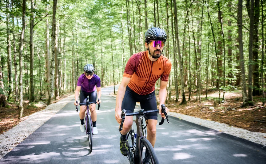 Due ciclisti con casco che pedalano su una strada nella foresta
