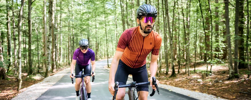 Zwei Radfahrer in Schutzhelmen fahren auf einem Waldweg