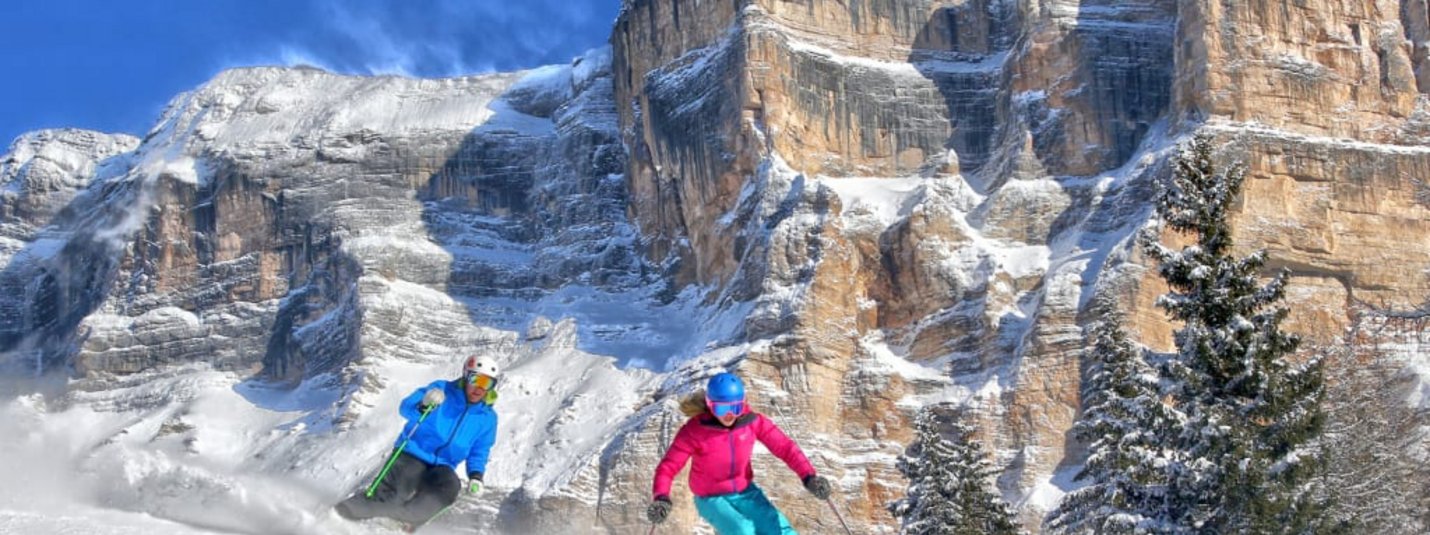 Two skiers skiing on snowy slope with rocky mountains in background