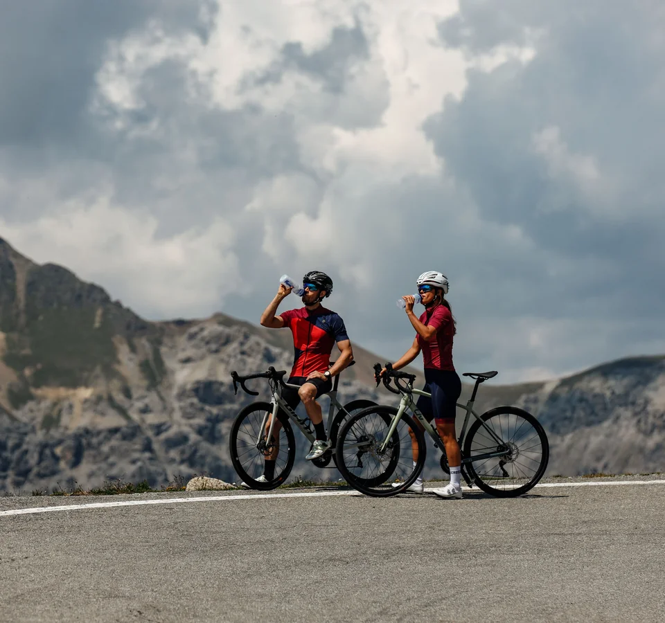 Endless adventures in the Nauders–Reschensee region © Felix Saller Two cyclists drinking water on a mountain road under cloudy sky