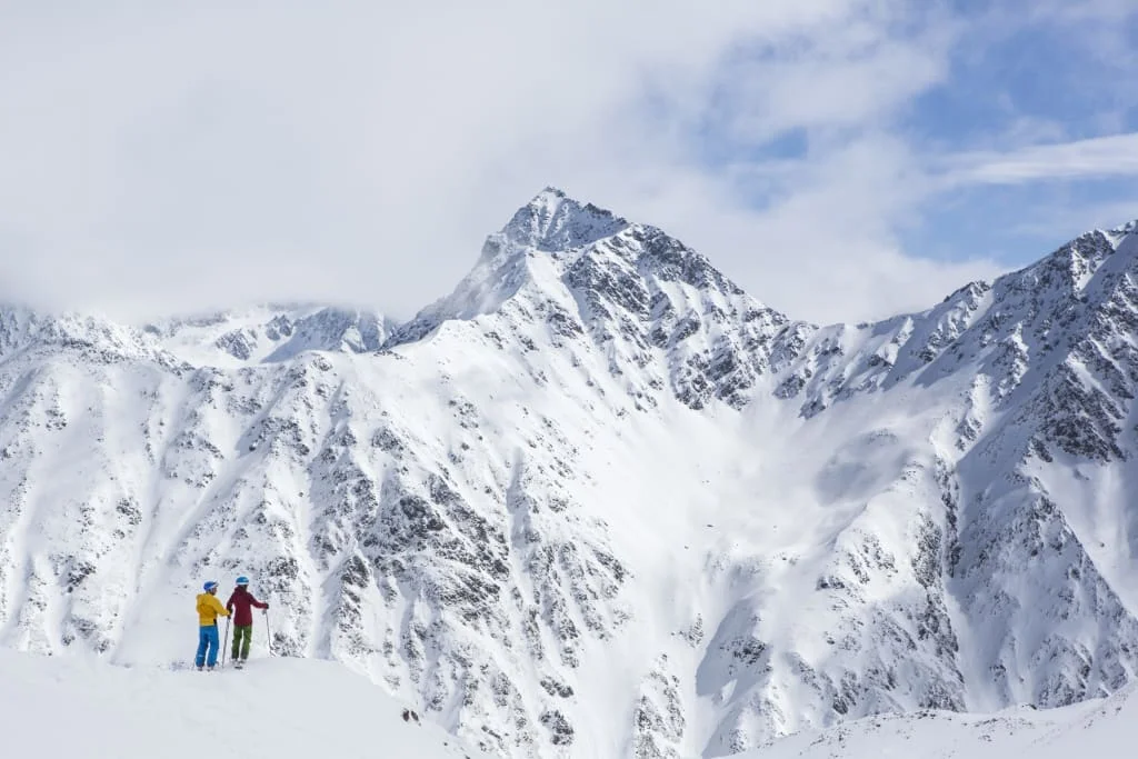 Zwei Skifahrer auf schneebedecktem Berg mit hoher Bergspitze im Hintergrund
