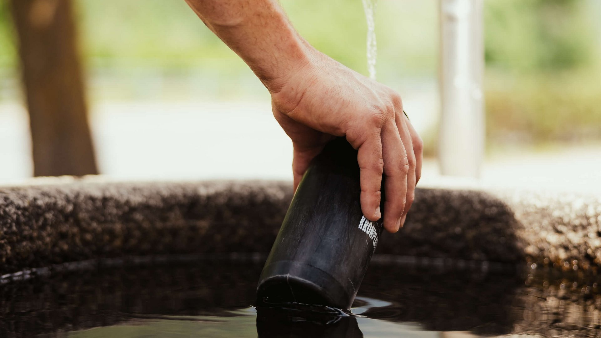 Hand füllt Flasche aus Metall unter Wasserhahn im Freien