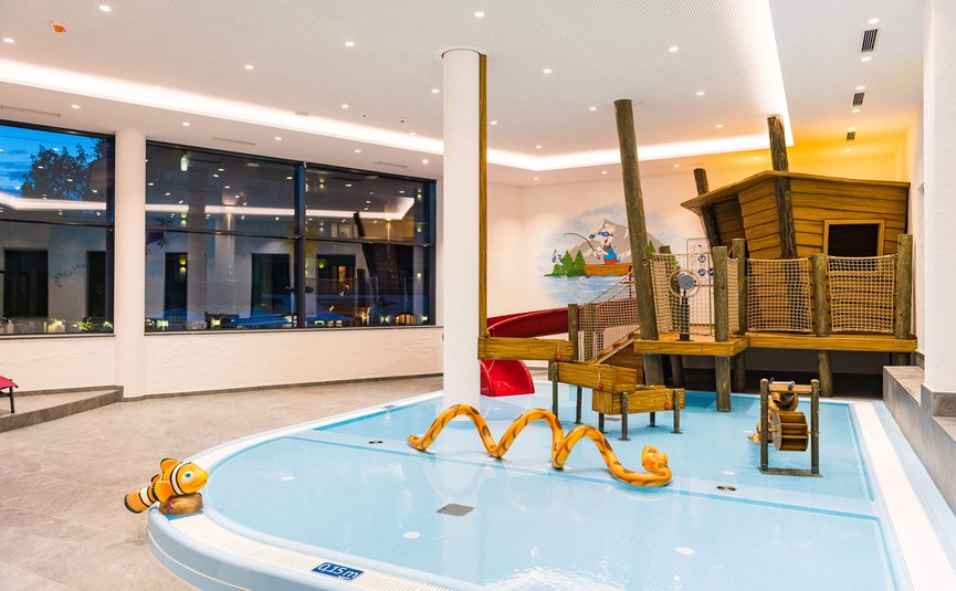 Children's play area with shallow pool and wooden slide structure indoors