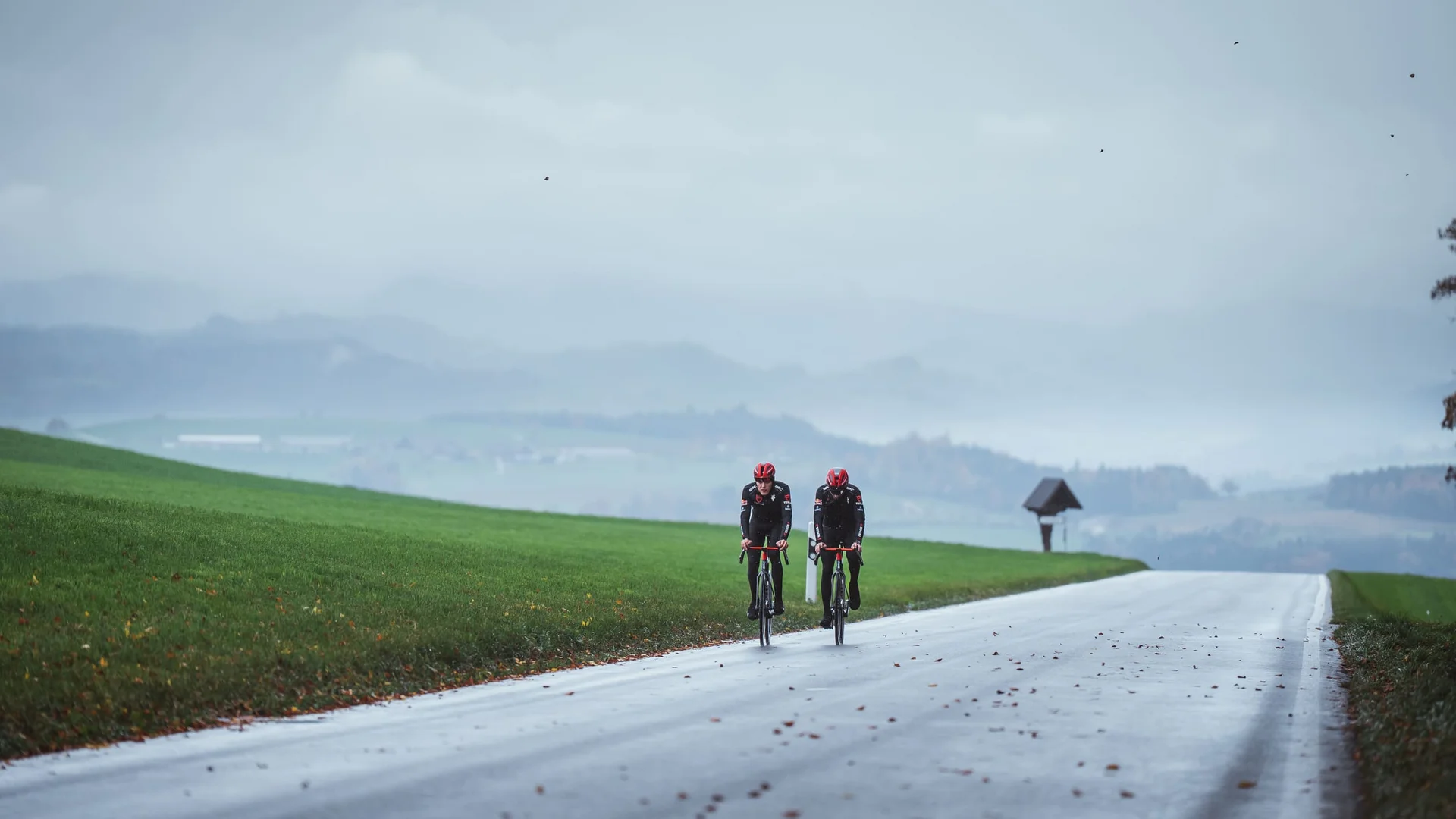 Schwalbe One 365 © Ralf Bohle GmbH Zwei Radfahrer fahren auf einer nassen Landstraße durch eine neblige Hügellandschaft