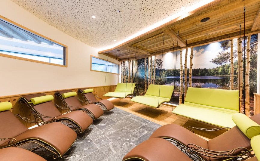 Sala relax con sdraio marroni e sedie sospese verdi davanti a murale bosco