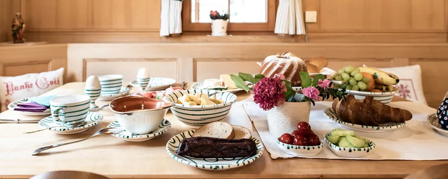 Gemütlicher Frühstückstisch mit Brot, Obst und Butter in traditioneller Holzstube