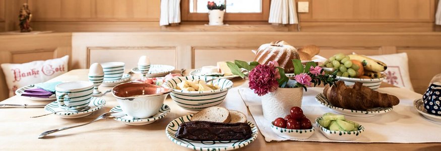 Gemütlicher Frühstückstisch mit Brot, Obst und Butter in traditioneller Holzstube