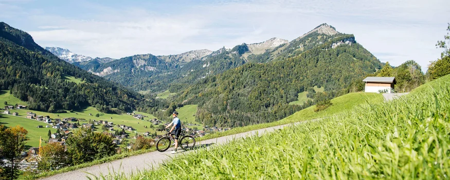 Fahrradfahrer auf Bergstraße mit Alpen und Dorf im Hintergrund