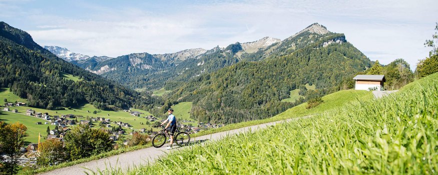 Hotel Bären & Café Deli *** © Alex Kaiser Fietser op bergweg met Alpen en dorp op de achtergrond