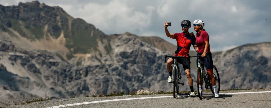 Two cyclists take a selfie on mountain road with mountains behind