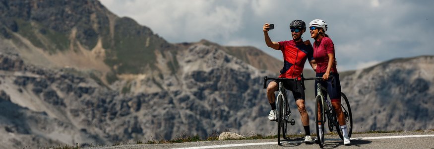 Twee fietsers maken een selfie op een bergweg met bergen op de achtergrond