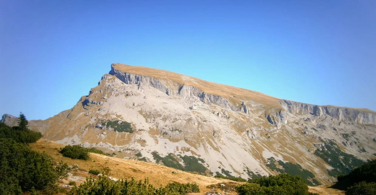 Felsiger Berg mit grasbewachsenem Hang unter blauem Himmel