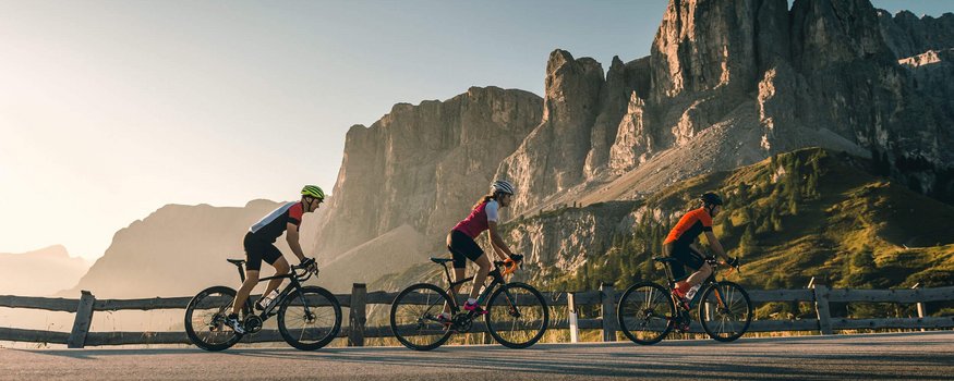 Drie fietsers fietsen op bergweg met rotskliffen bij zonsondergang