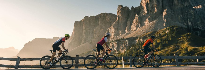Drei Radfahrer fahren auf Bergstraße mit Felsen im Hintergrund bei Sonnenuntergang