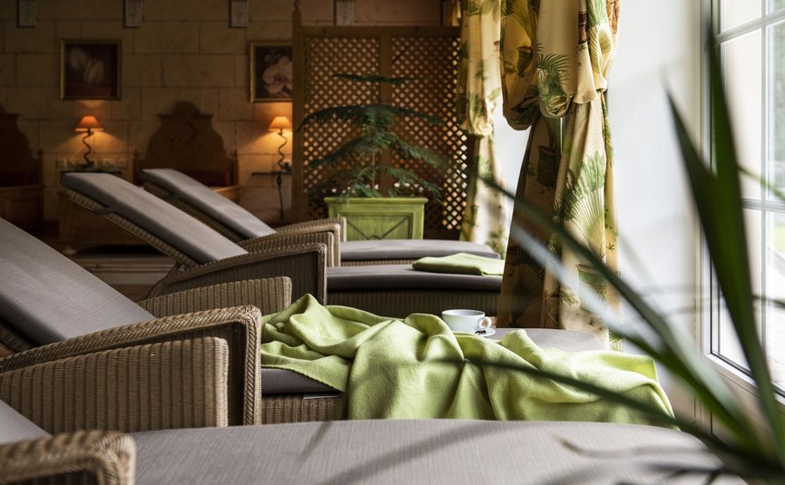 Lounge chairs with green blanket and cup beside window in a spa room