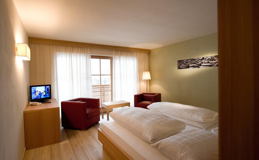 Gemütliches Hotelzimmer mit Doppelbett, zwei Sesseln und TV