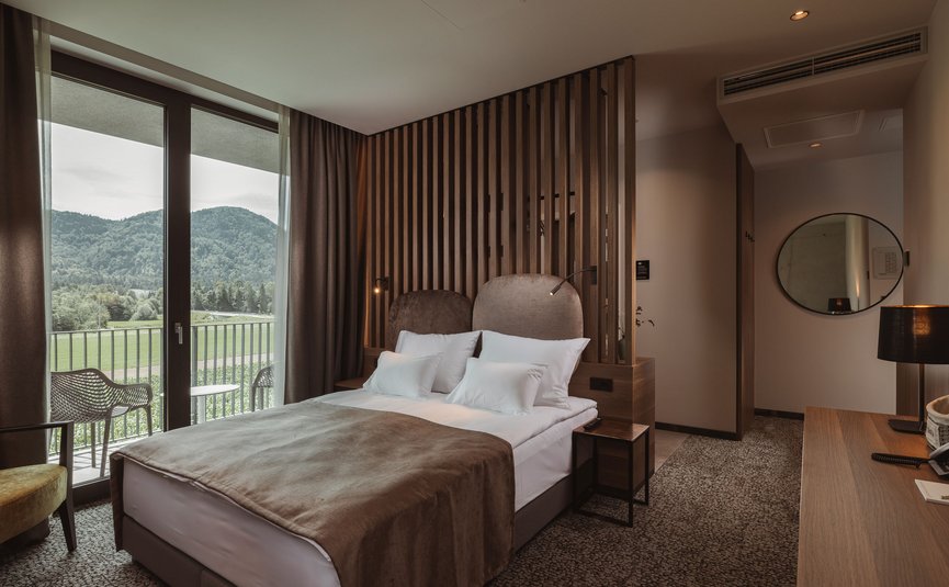 Camera d'albergo moderna con letto matrimoniale e vista montagna dalle finestre a tutta altezza