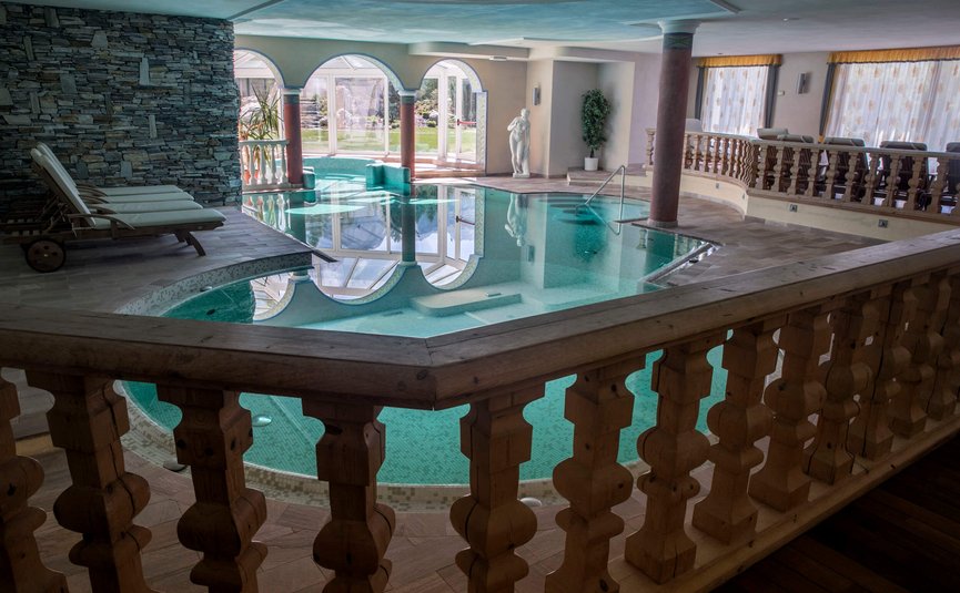 Innenpool mit Liegestühlen, Säulen und Statue in luxuriösem Spa-Bereich
