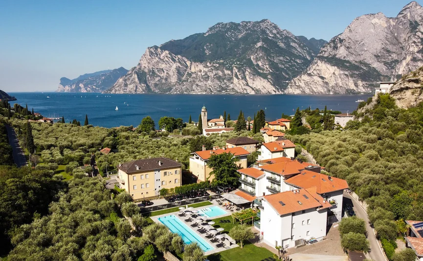 Vista di un lago con montagne e un villaggio con piscine e uliveti