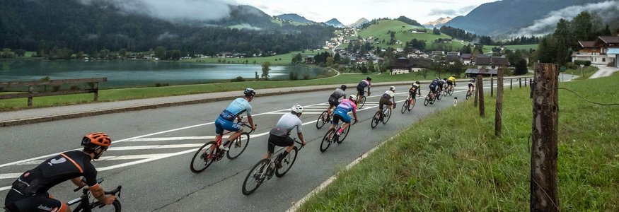 Groep wielrenners op een weg met bergen en meer op de achtergrond