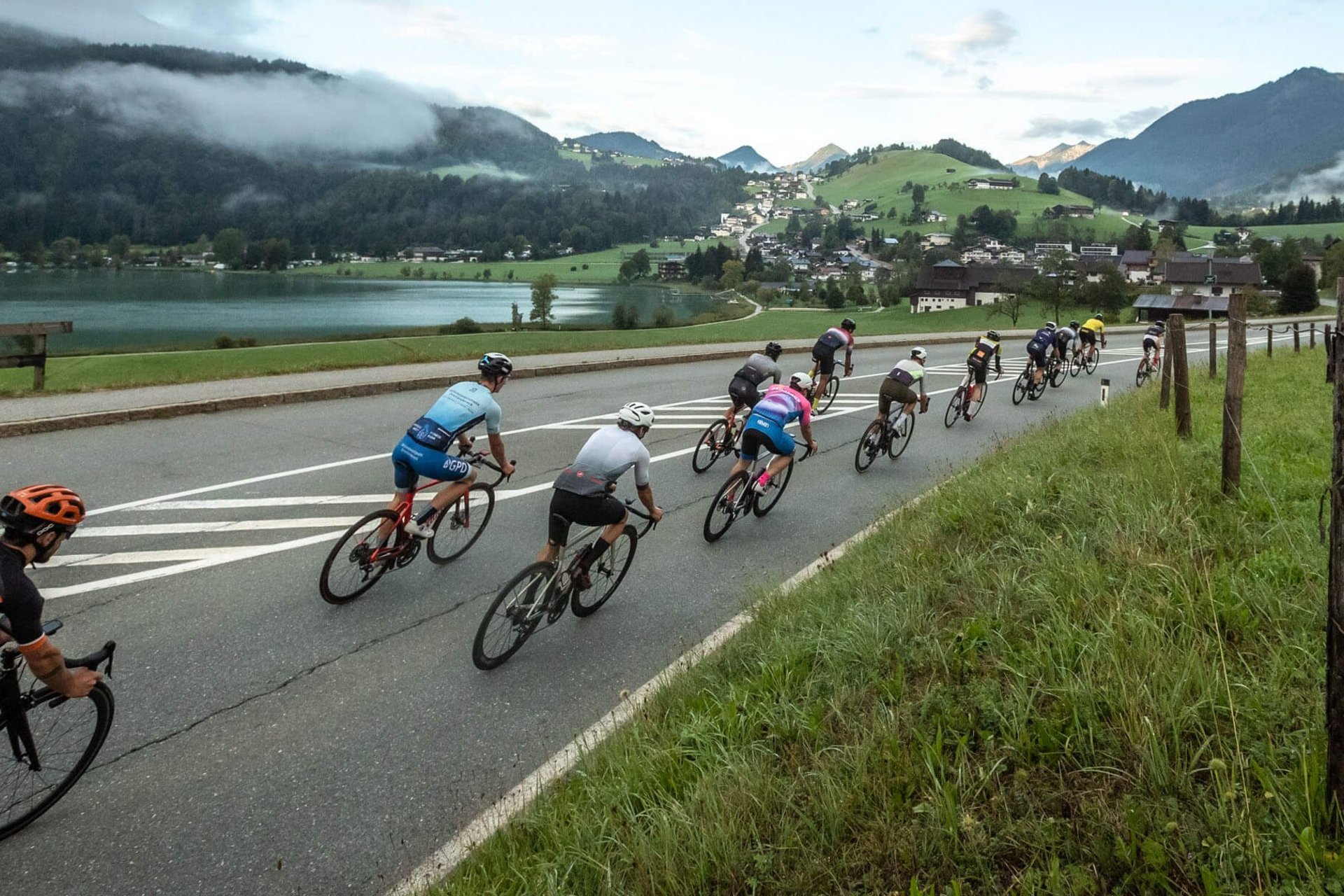 Gruppo di ciclisti su strada con montagne e lago sullo sfondo