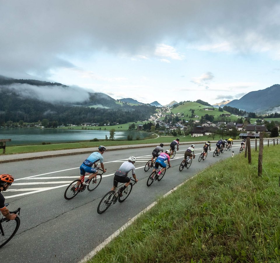 Kufsteinerland Fiets Marathon © Erwin Haiden Groep wielrenners op een weg met bergen en meer op de achtergrond