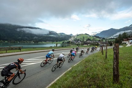 Groep wielrenners op een weg met bergen en meer op de achtergrond