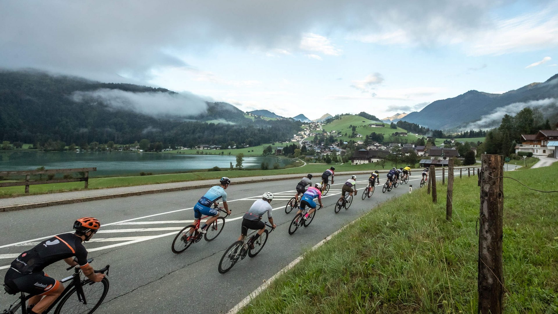 Gruppe von Radfahrern auf einer Straße mit Berg- und Seelandschaft