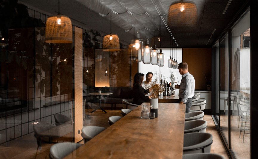 Tre persone in un elegante bar con tavolo di legno e luce soffusa