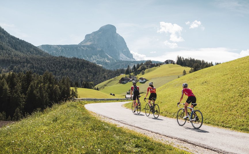 Three cyclists riding on a mountain road with alpine scenery