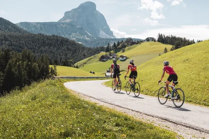 Drei Radfahrer fahren auf einer Bergstraße mit Alpenpanorama