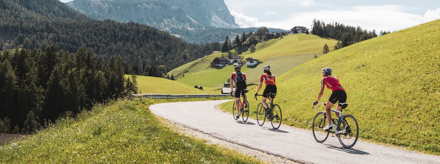 Three cyclists riding on a mountain road with alpine scenery