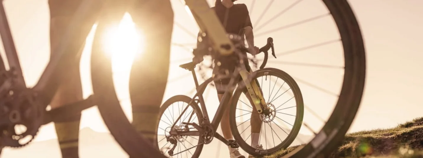 LUXUS Gravel Package Fahrradfahrer mit Helm und Sonnenbrille bei Sonnenuntergang auf Grasland