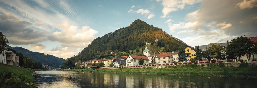 Riva del fiume con case e collina boschiva sotto cielo nuvoloso