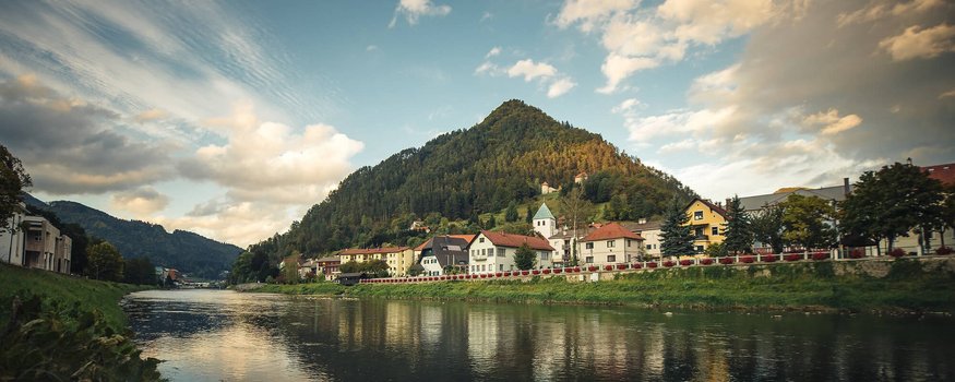Hotel Grof **** © Jacob Riglin - www.slovenia.info Riverbank with houses and wooded hill under cloudy sky