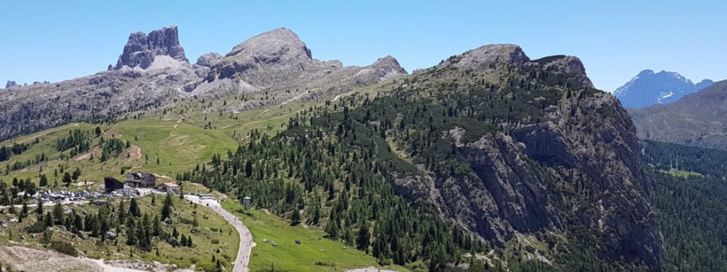 Paesaggio montano con strada tortuosa e prati verdi sotto cielo azzurro