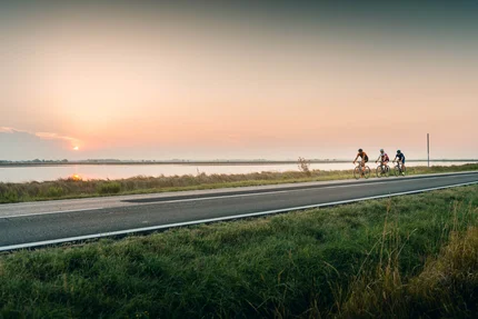 Drie wielrenners fietsen langs een rivier bij zonsondergang