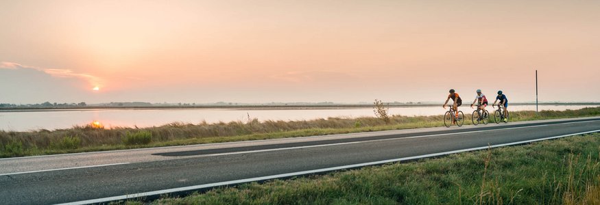 Three cyclists riding by a river at sunset