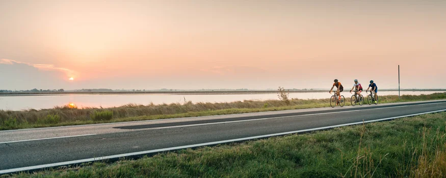 Costa adriatica © Alex Moling Tre ciclisti che pedalano lungo un fiume al tramonto