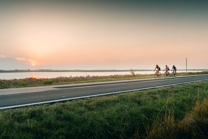 Drei Radfahrer fahren bei Sonnenuntergang an einem Fluss entlang