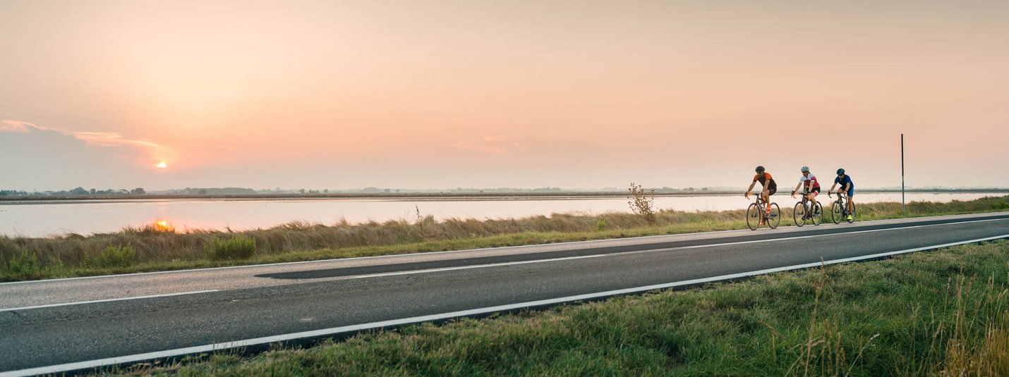 Three cyclists riding by a river at sunset