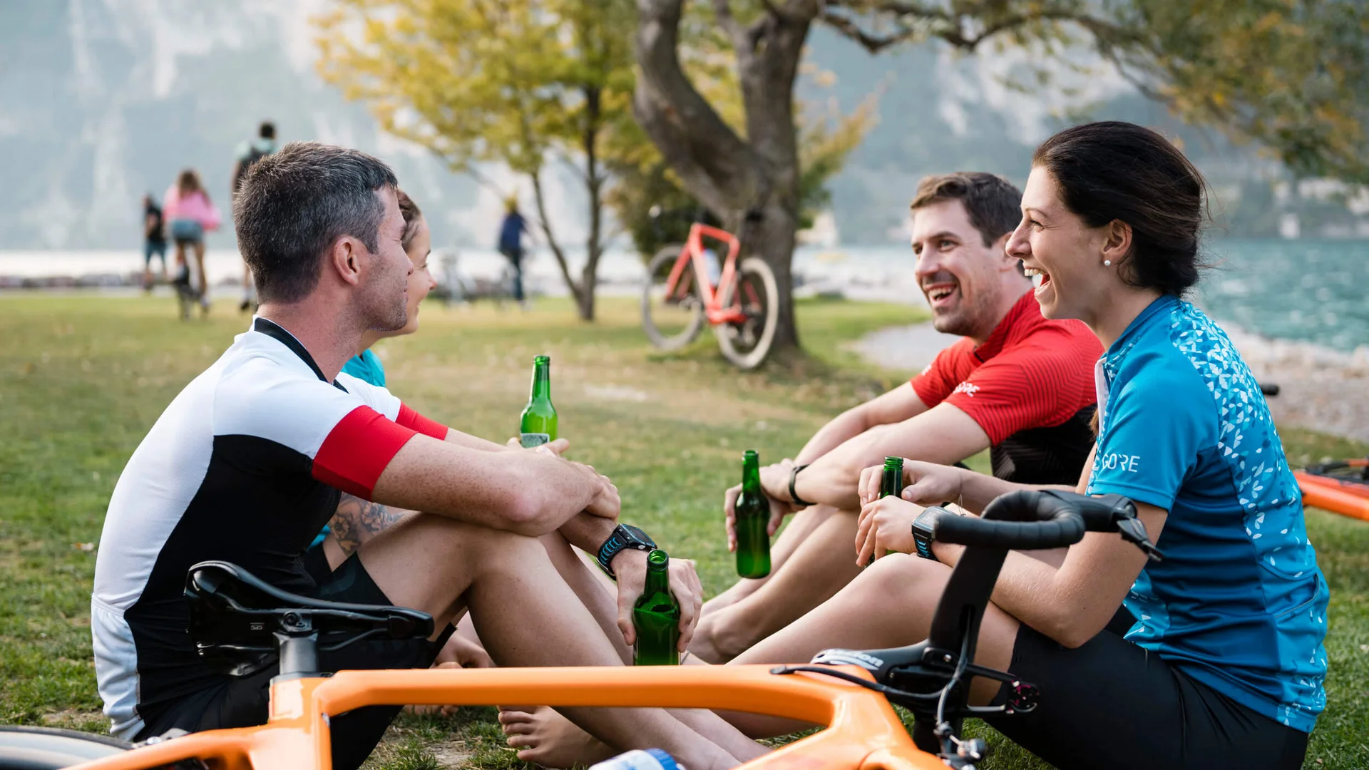 Gruppe von Radfahrern sitzt auf Gras und trinkt Bier am See