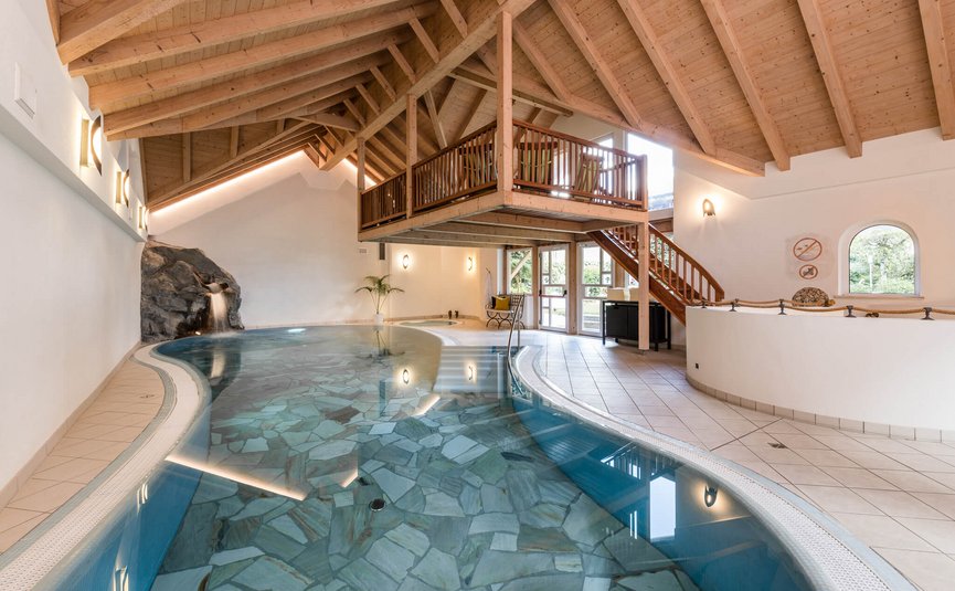 Indoor pool with waterfall and wooden ceiling under mezzanine