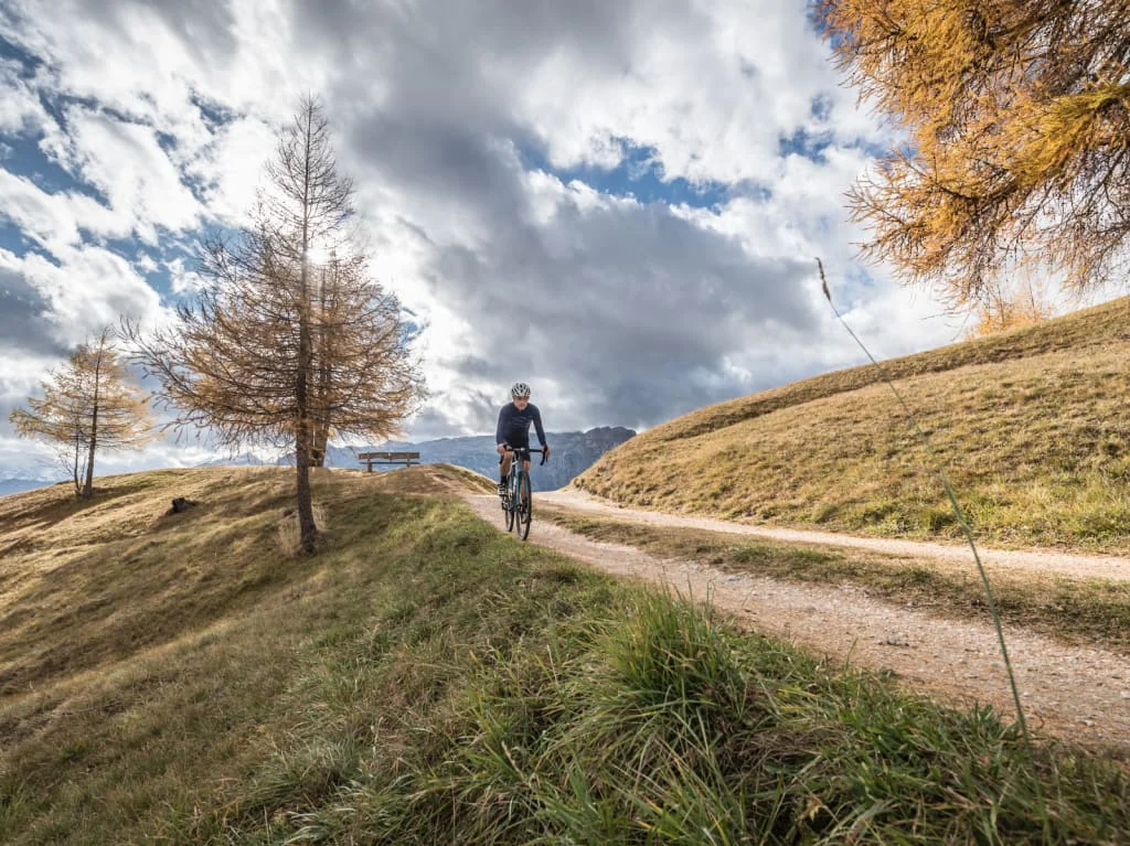 Ciclista su un sentiero in paesaggio montano autunnale sotto cielo nuvoloso