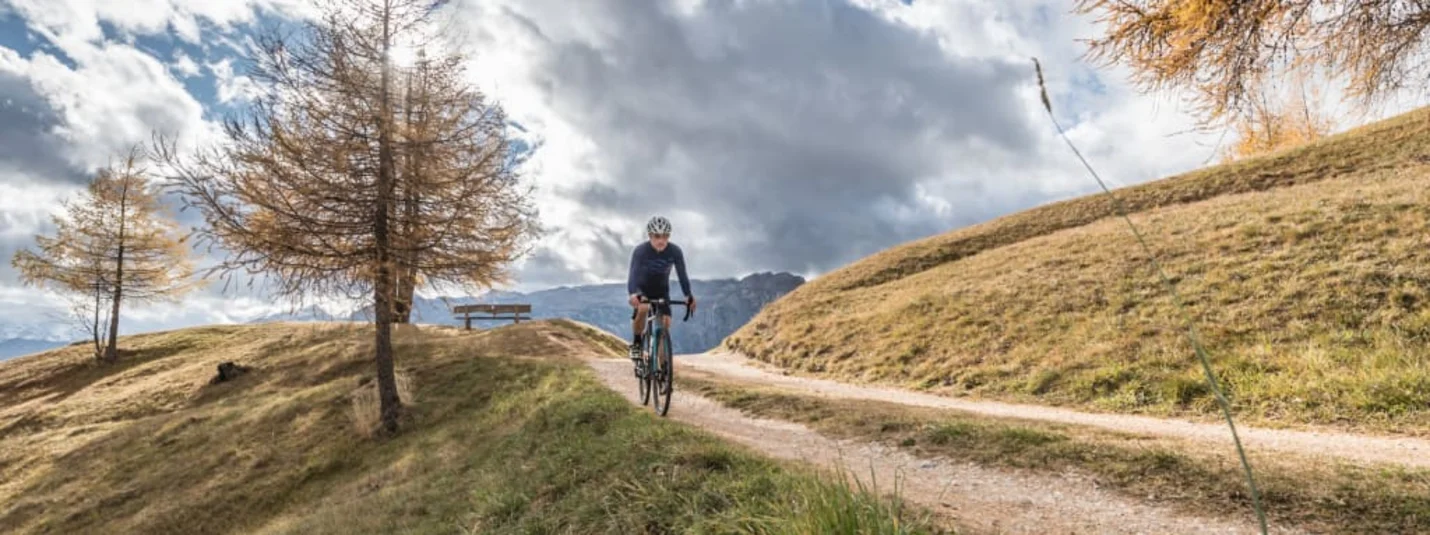 Gravel Bike Short Stay - 5 nights Ciclista su un sentiero in paesaggio montano autunnale sotto cielo nuvoloso