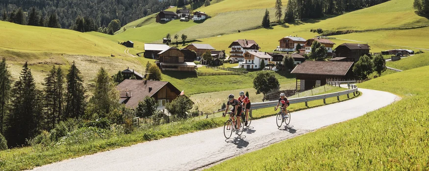 Radfahrer auf Landstraße mit Berg und Dorf im Hintergrund