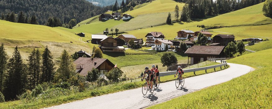 Zwischen Pass & Pasta in San Vigilio © Alex Moling Radfahrer auf Landstraße mit Berg und Dorf im Hintergrund