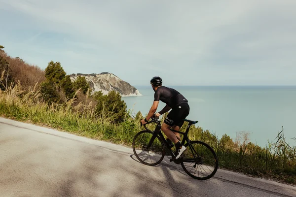Cyclist on road with sea view and hills in the background
