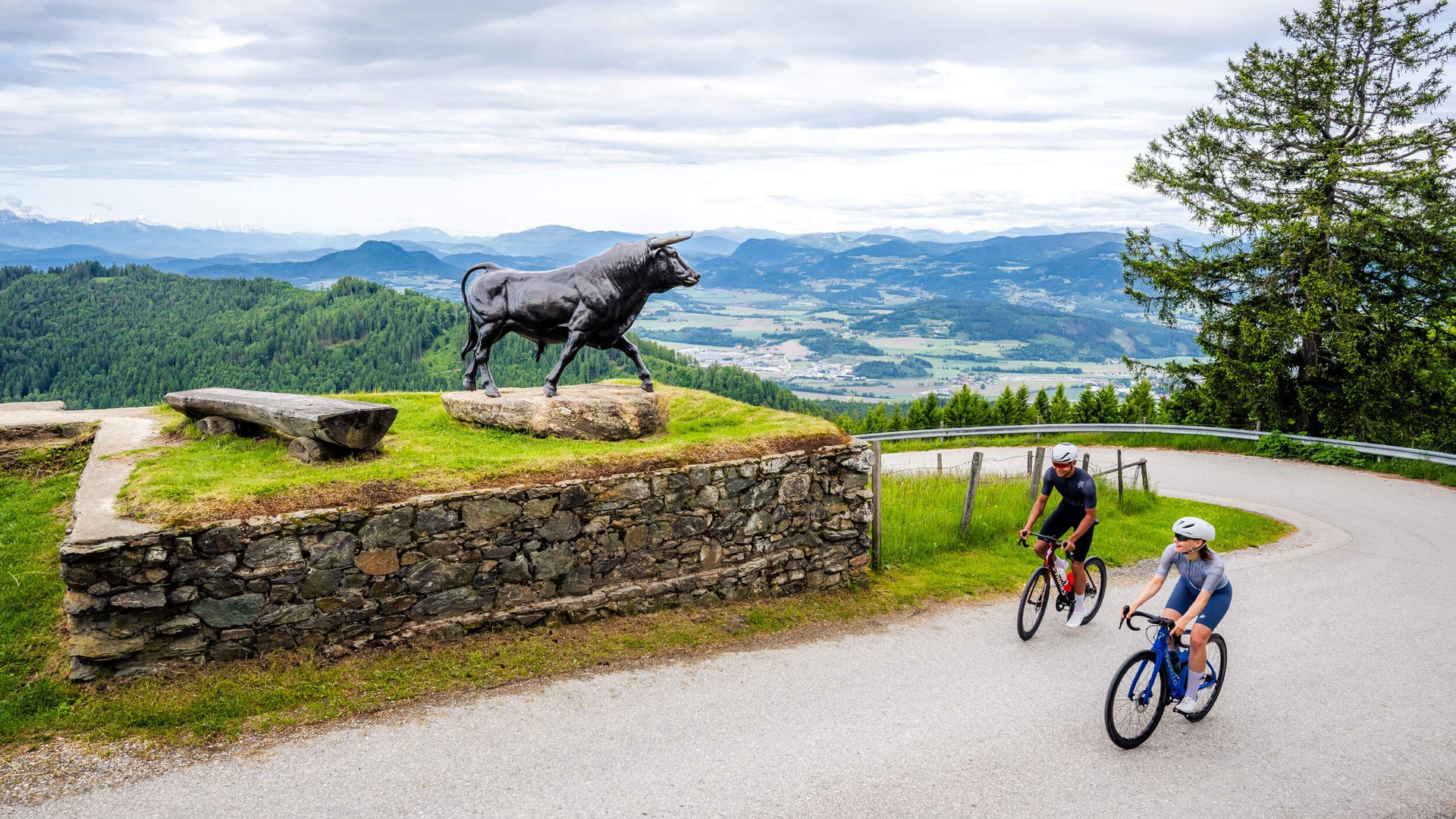 Zwei Radfahrer fahren an einer Stierstatue auf einer Bergstraße vorbei
